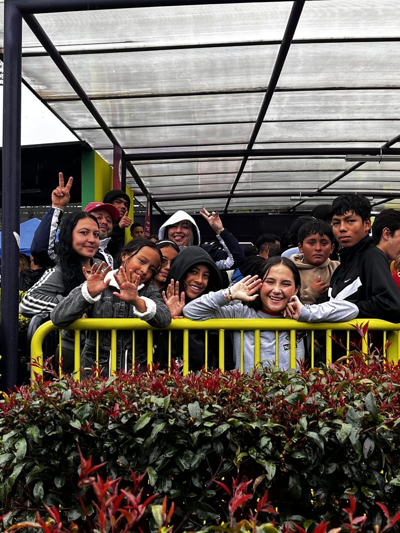 Un grupo de adolescentes y adultos sonríe y saluda detrás de una baranda amarilla, bajo una cubierta, durante una actividad de la fundación.
