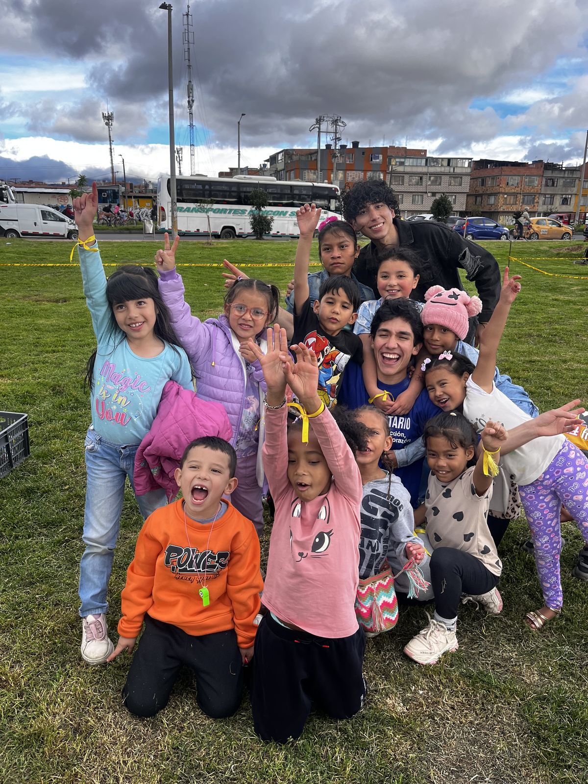 Un grupo de niños y niñas celebra con los brazos en alto sobre el pasto de un parque, junto a jóvenes voluntarios de la fundación.