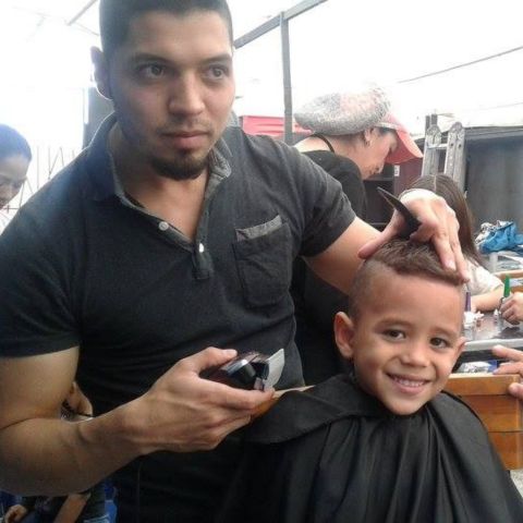 Un barbero le corta el cabello a un niño que sonríe durante una jornada de la fundación.
