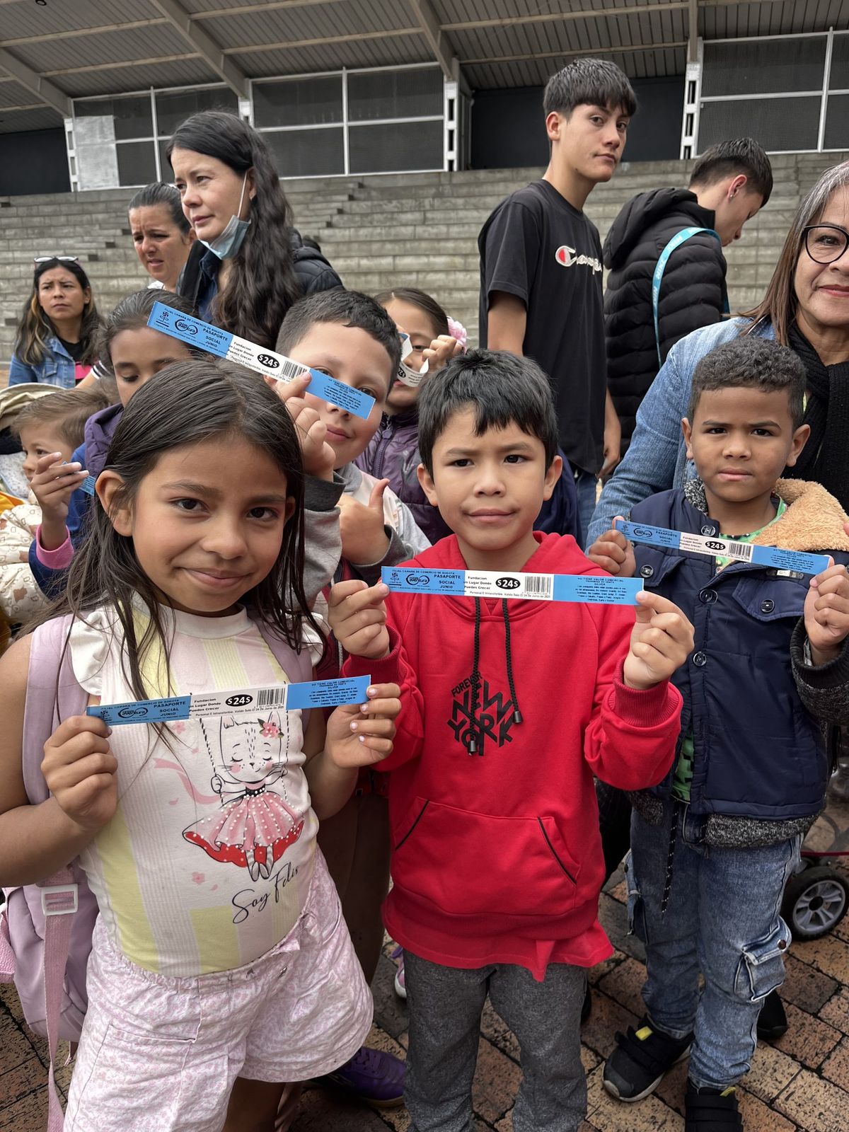 Niños y niñas muestran sus manillas azules del «Pasaporte social» de Mundo Aventura, a nombre de la fundación, junto a jóvenes y adultas que los acompañan.