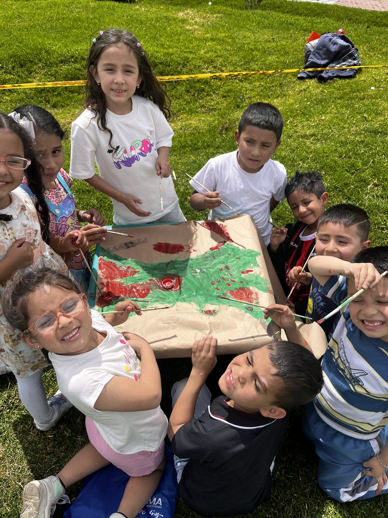 Un grupo de niños y niñas pinta en círculo sobre el pasto durante un taller al aire libre.
