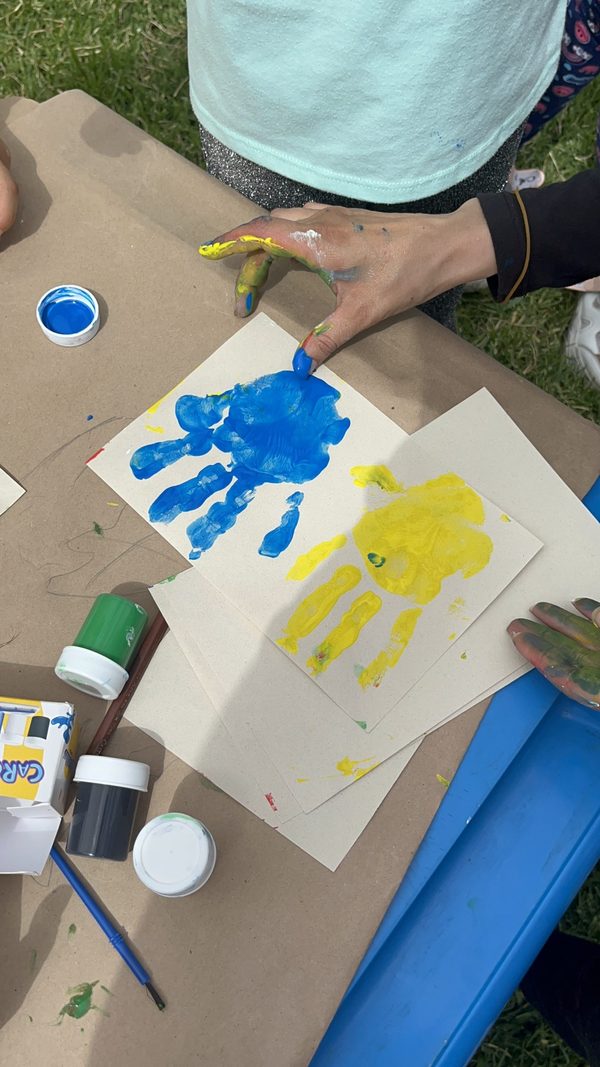 Las manos de un niño estampan huellas de pintura azul y amarilla sobre papel en un taller de arte de la fundación.