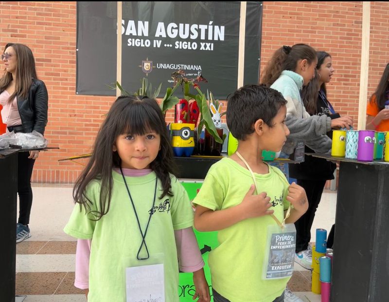 Dos niños con camisetas verdes de la fundación participan en una actividad educativa al aire libre, junto a una mesa con materiales.