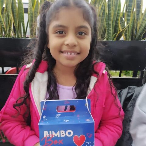 Una niña sonríe mientras sostiene una caja de alimentos.