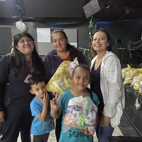Tres mujeres y dos niños sostienen bolsas con alimentos y productos de aseo durante una entrega de la fundación.
